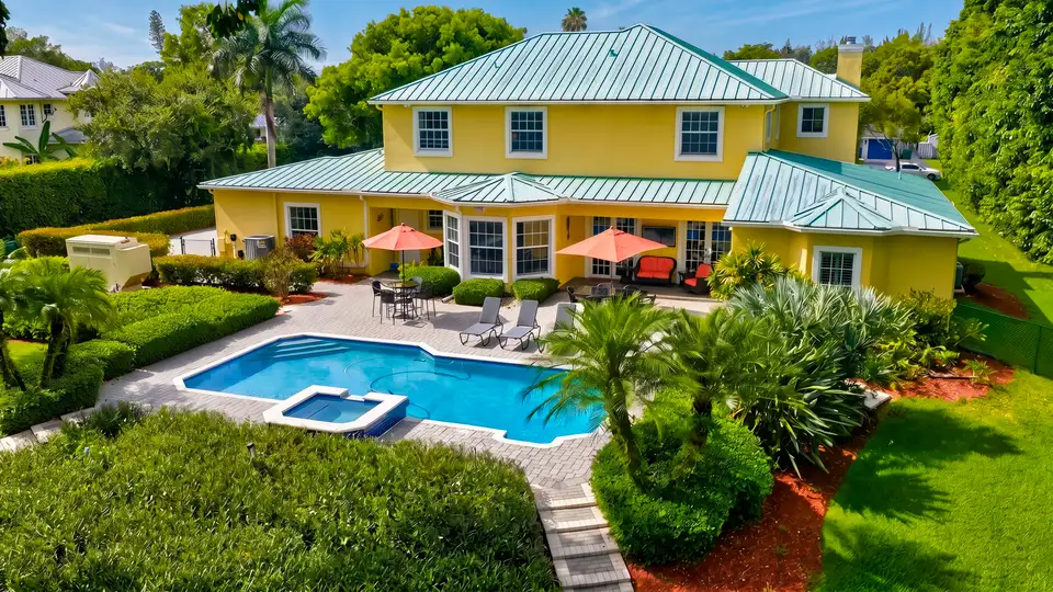 Drone photo of a two-story Broward County home with a pool, spa and paved patio