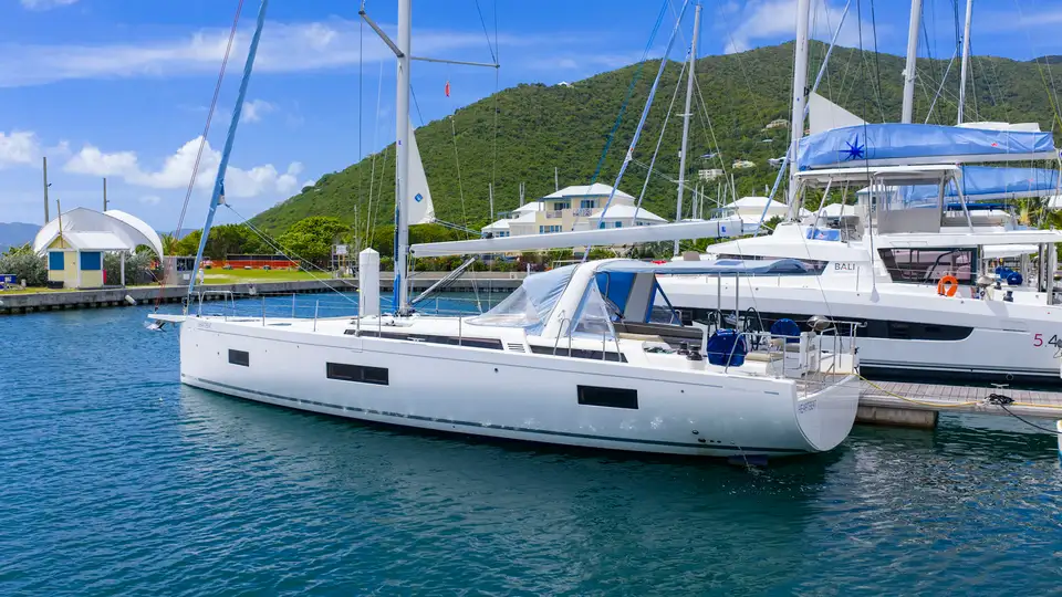 Sailing yacht at a marina dock with green hills behind, photographed for a broker listing