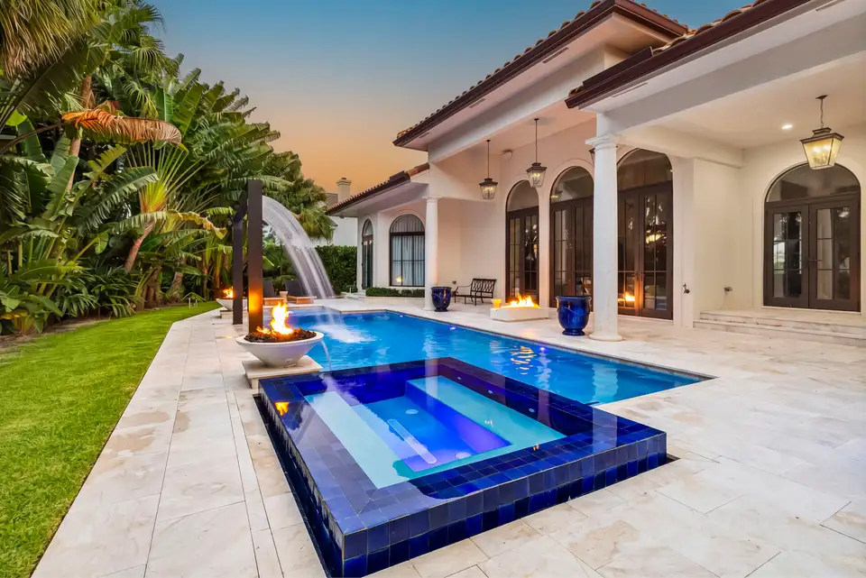 Twilight photo of a pool and spa with fire bowls lit and arched doors glowing at dusk